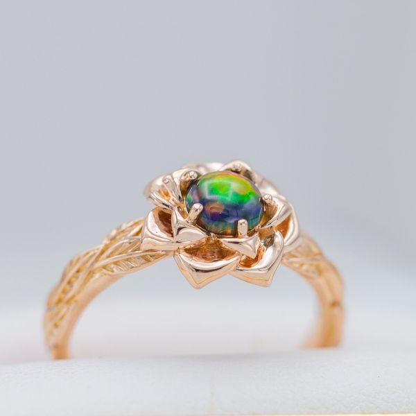 The lab-created black opal at the heart of this rose ring shows intense color play.