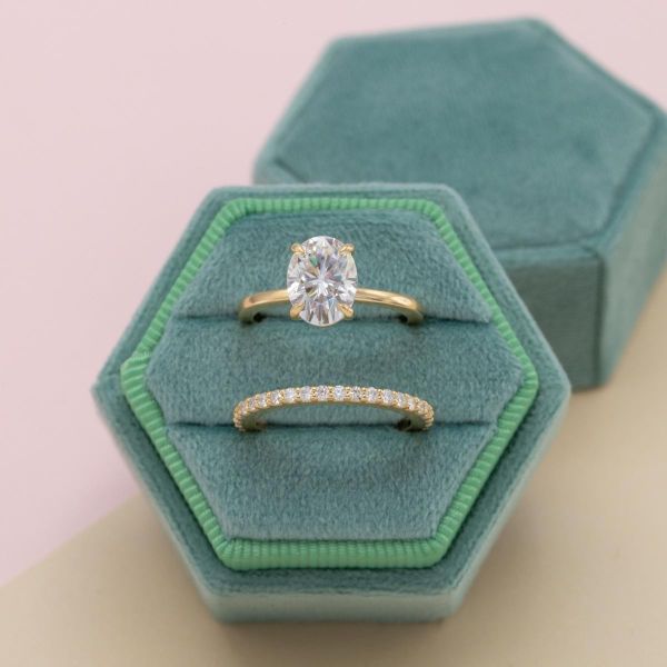 An oval moissanite takes center stage in this simple yellow gold engagement ring with a matching pave wedding band.