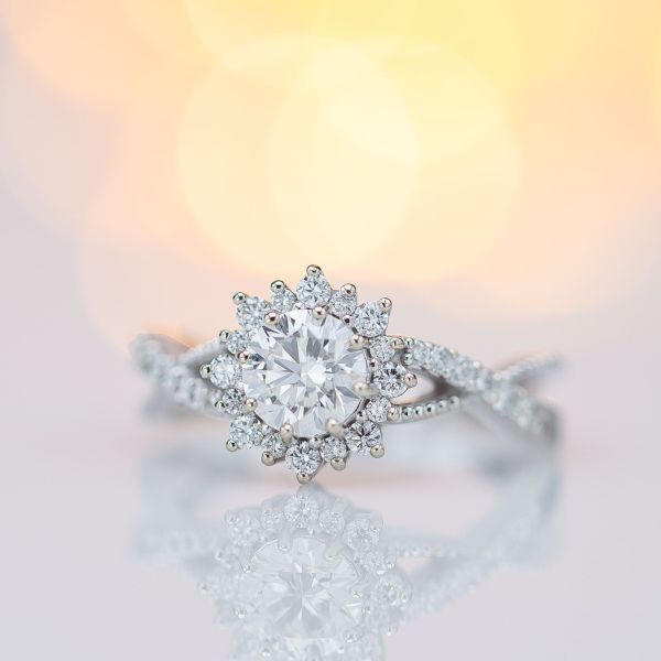 A vining band and delicate sunburst halo accentuate the perfect hearts & arrows diamond in this engagement ring.