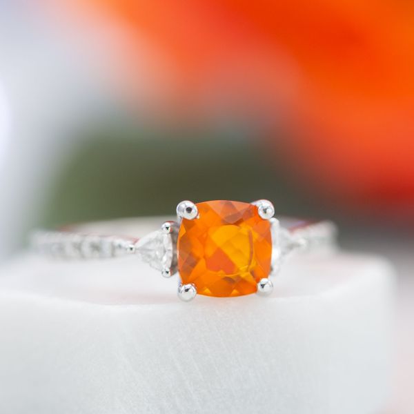 The vivid, fiery red of this fire opal draws the eye as the center stone of a contemporary, three-stone engagement ring.