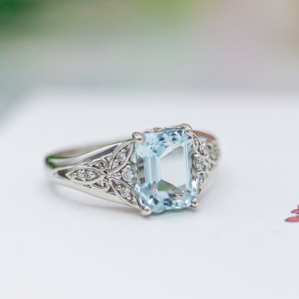 Vintage-inspired engagement ring with emerald cut aquamarine and open shoulder details hinting at a dragonfly.