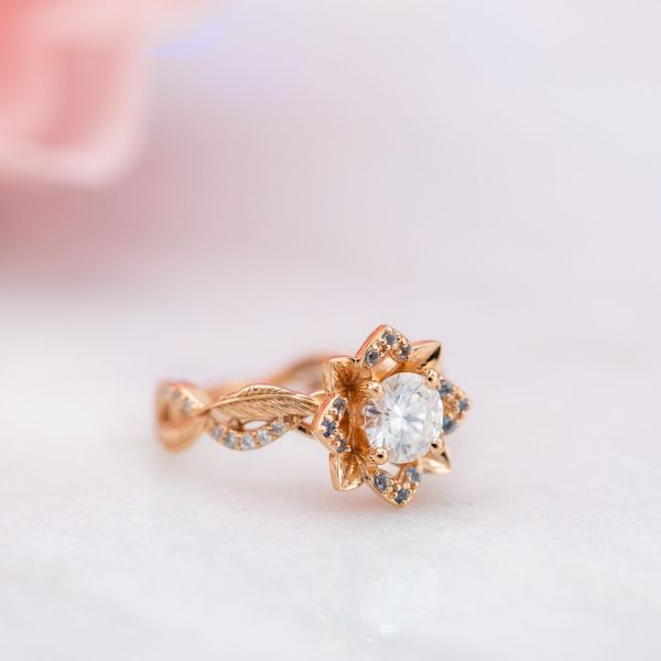Rose gold and moissanite lotus engagement ring with quills along the band and aquamarine accents.