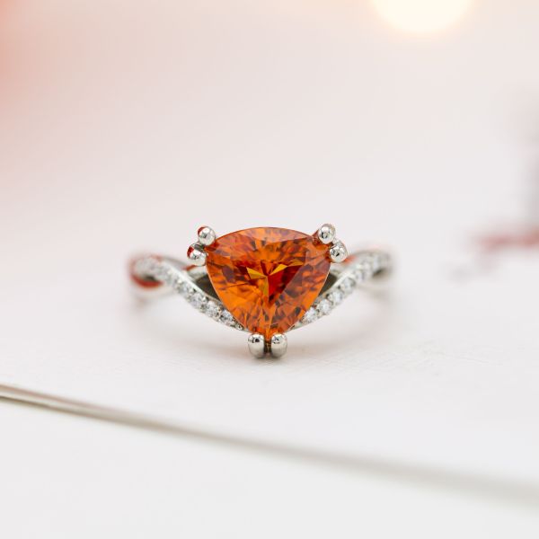 An incredible, vivid orange sapphire engagement ring with a delicate, twisting band with diamond pave.