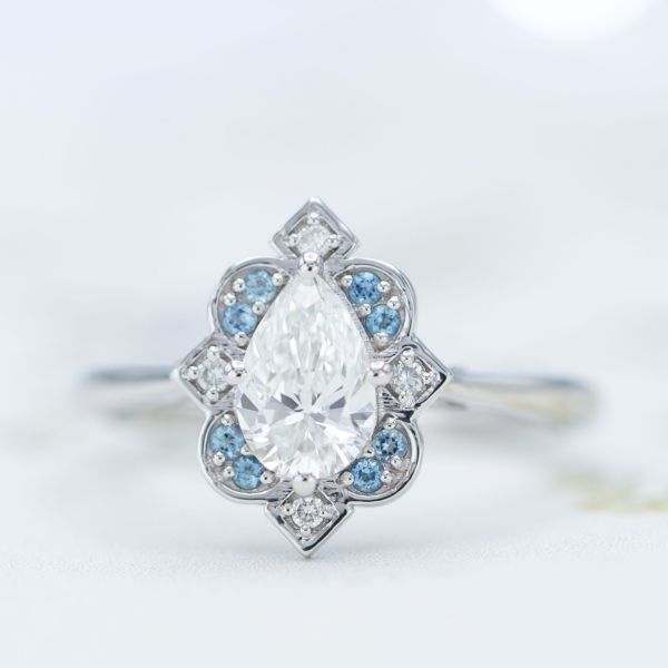 A pear cut center stone in an Art Deco-inspired antique frame halo with aquamarines and diamonds.