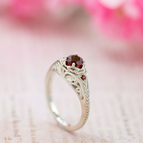 Vintage-inspired garnet engagement ring with floral setting and Deco-inspired chevron band.