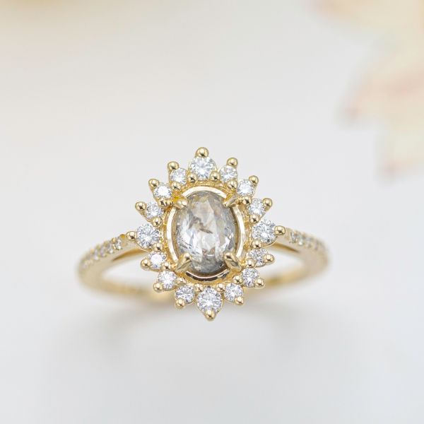 A salt and pepper, rose cut diamond is framed by a gold sunburst halo for a unique engagement ring design.