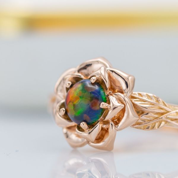 A lab-made opal shows its vivid blues, greens and oranges at the heart of this rose engagement ring.