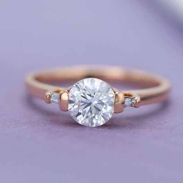 This three stone engagement ring uses bright, open bar settings for the round center stone and baguette side stones.