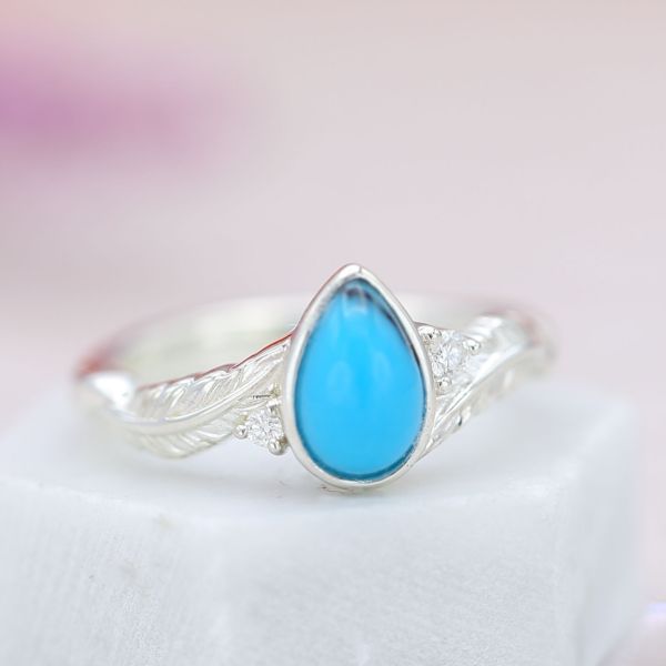 Feather engagement ring with a pear cut turquoise center stone and diamond accents.