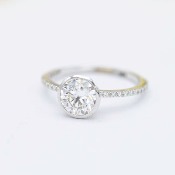 This delicate engagement ring uses a bezel setting for the center moissanite for a sleek, sparkly look.