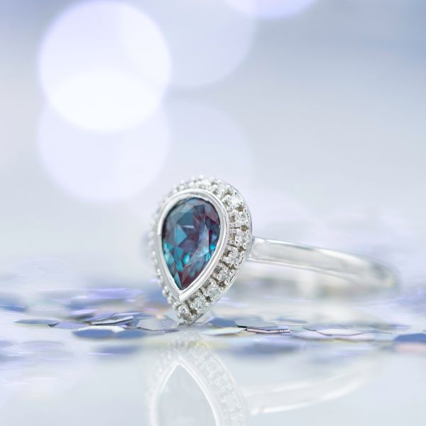 Lab-created alexandrite and diamond halo ring with a pear cut center stone.