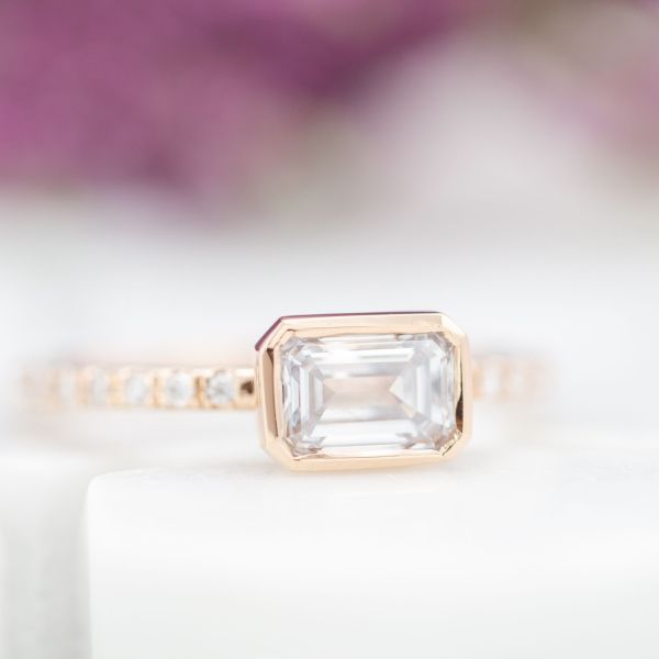 A delicate, east-west set diamond engagement ring with an east-west set emerald cut center stone.