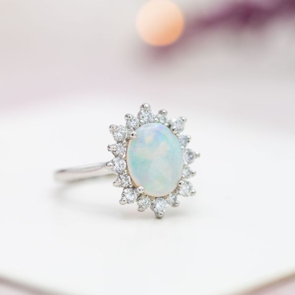 A sunburst halo creates the look of a snowflake around the cool blues and greens of this ring's opal center stone.