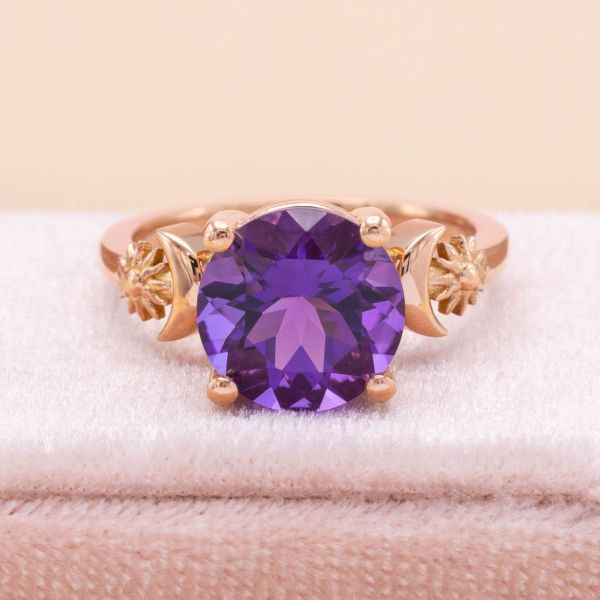 Rose gold suns and moons hold a brilliant round amethyst.