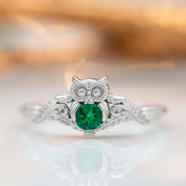 Owl engagement ring in white gold with an emerald center stone and feather detailing on the band.