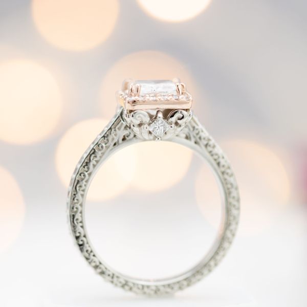 A small, princess cut peek-a-boo gem is tucked on the side of this engagement ring's center setting.