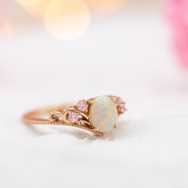 A beautiful white opal showcases the stone's distinctive color play in this vintage-inspired rose gold ring.