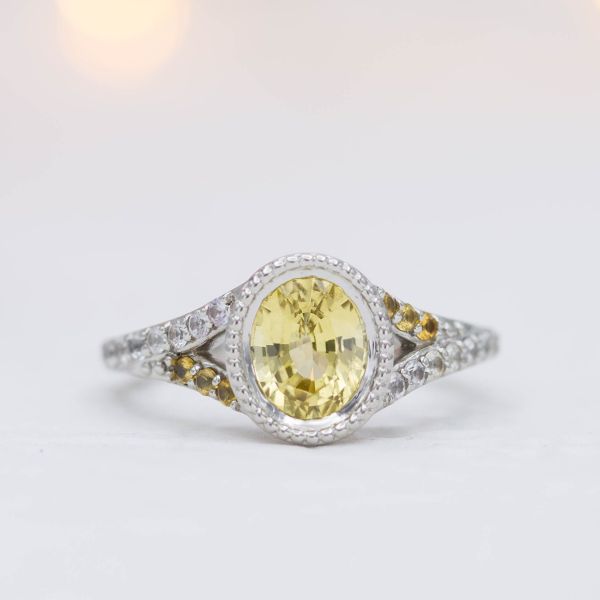 Oval canary yellow sapphire engagement ring with beaded edges on the bezel and a split shank.