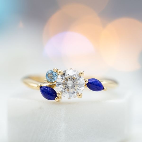 A delicate diamond engagement ring creates the feel of flowing water with a cluster of lapis and aquamarine.