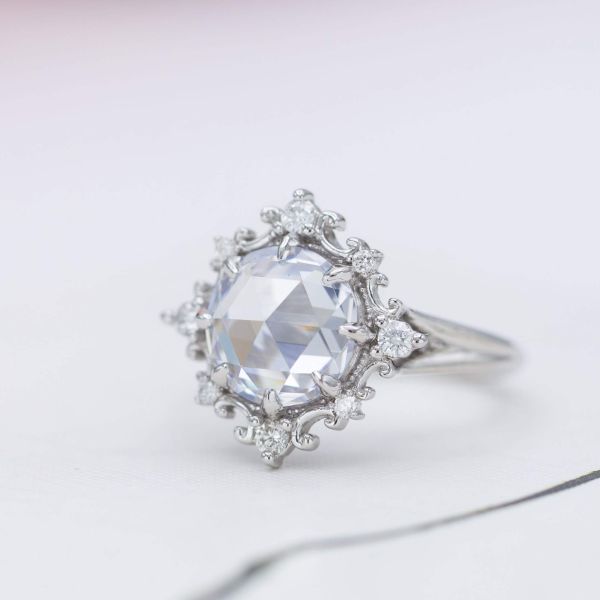 Vintage-inspired engagement ring with a delicate, intricate halo framing a large rose cut diamond.