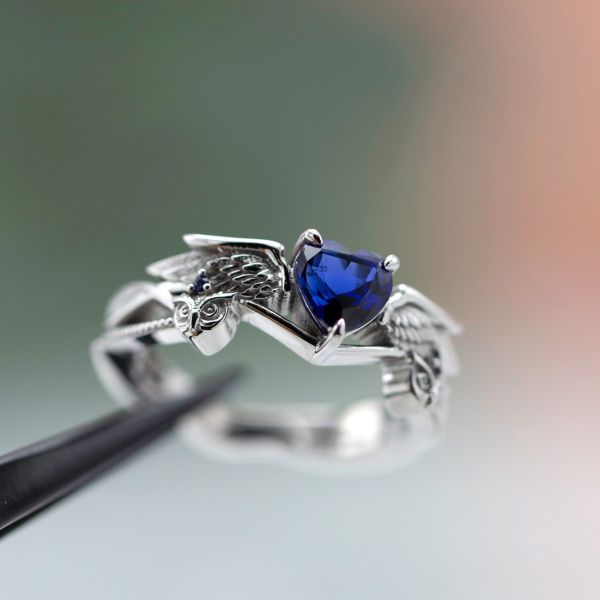 A heart shaped sapphire engagement ring with owls and wings framing the center setting.