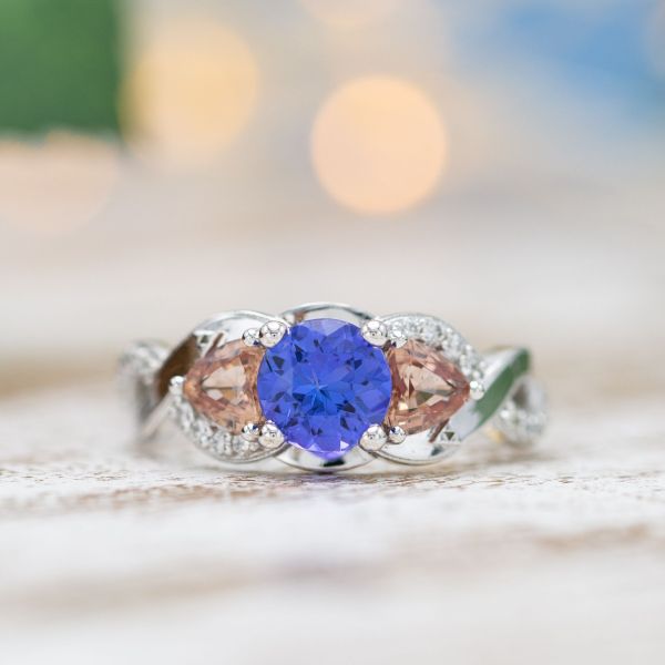 Tanzanite and Padparadscha sapphire in a three-stone engagement ring with a twisting band.