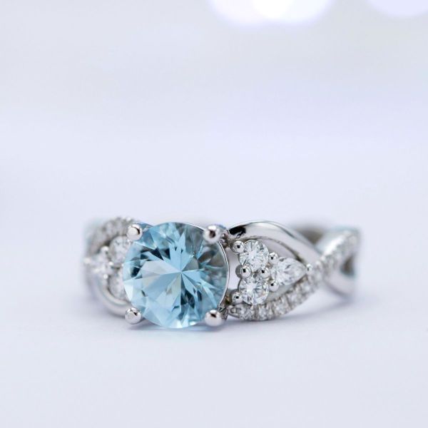 Aquamarine engagement ring with diamond clusters tucked into the curves of a twisting, pave band.