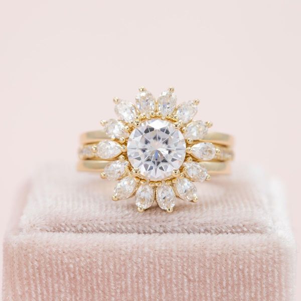 A bright white moissanite sits in the center of this sunburst halo engagement ring.