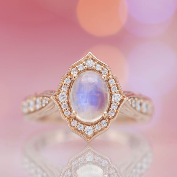 Rose gold and moonstone engagement ring with a petal-like halo curving around it.