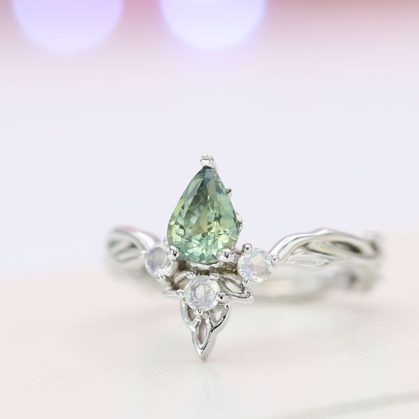A minty green sapphire engagement ring with a vining tiara inspiration and moonstone accents.