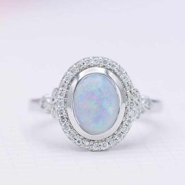 The bezel setting in this modern halo ring protects the white opal and adds a sleek design element to the ring.