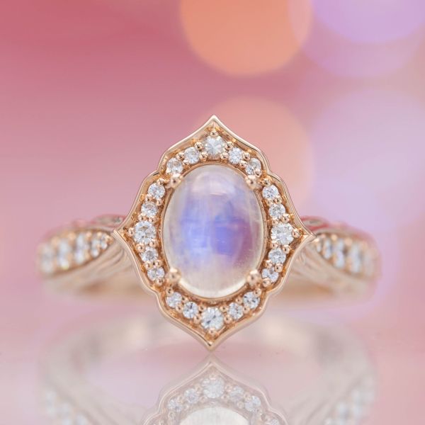 A delicately curving antique frame halo of diamonds surrounds an oval moonstone center stone.