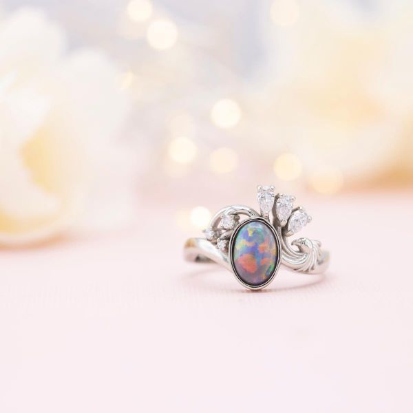 A knockout of a dark opal steals the show in this engagement ring, whose striking curves and diamond accents form a phoenix.