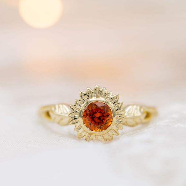 A gold sunflower engagement ring with the warm, vibrant orange of spessartite garnet at its center.
