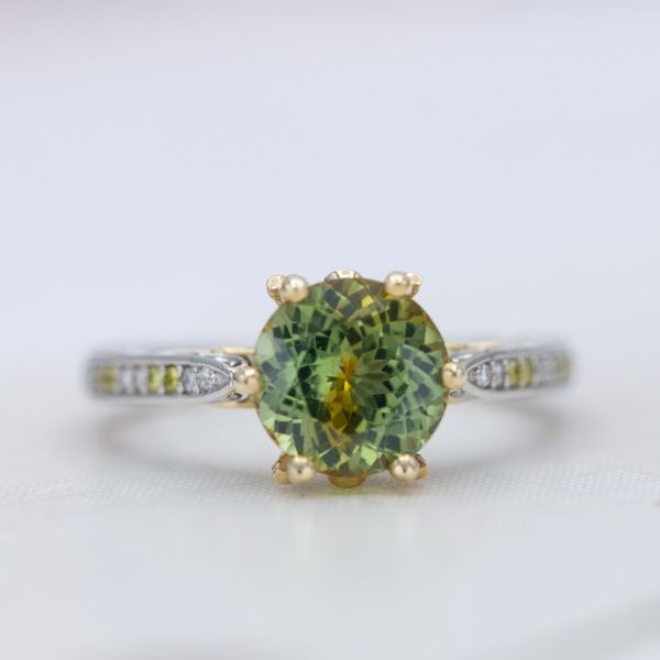 The gold basket of this engagement ring brings out yellow hues in the bright green sapphire center stone.