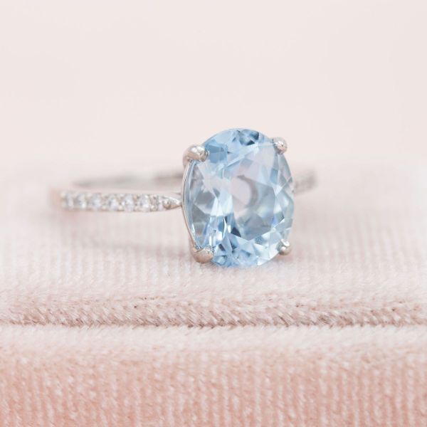 An oval aquamarine sits in the center of this solitaire setting with a band paved in diamond accents.
