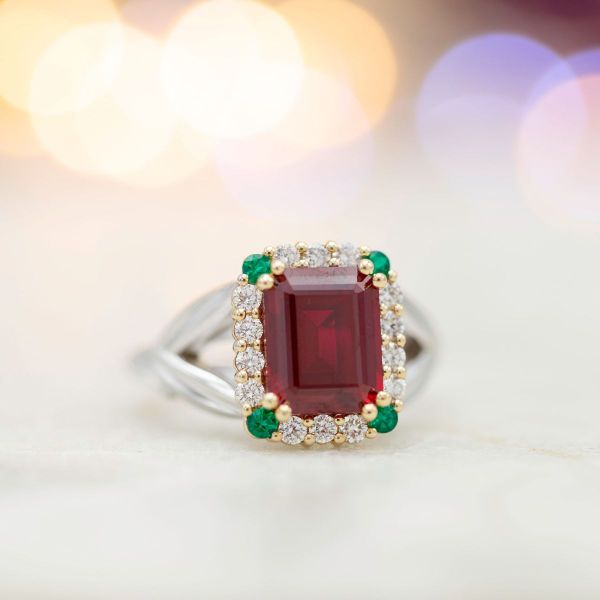Emeralds and diamonds combine to create a distinctive halo for this emerald cut ruby ring.