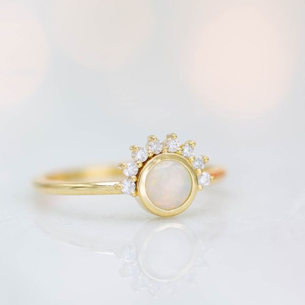 A sunburst-styled half halo surrounds the bezel set oval in this engagement ring.