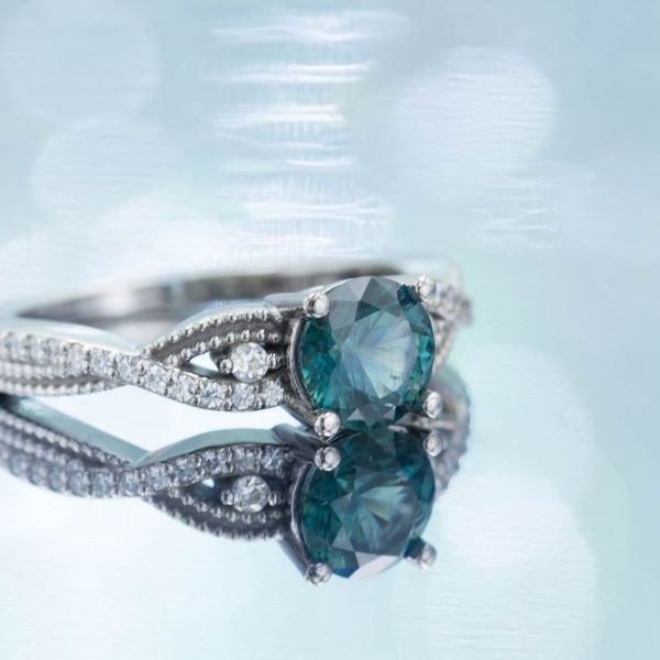 This teal-blue sapphire engagement ring has a twisting band and diamond accents.