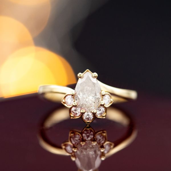 A salt and pepper diamond engagement ring with a petal half-halo and curving band.