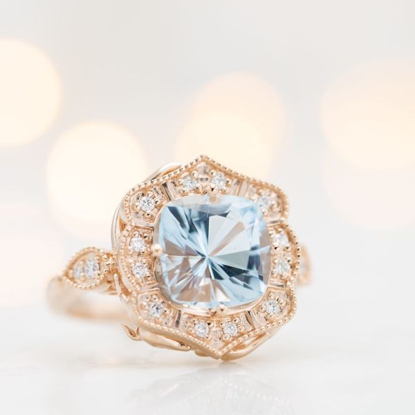 Rose gold engagement ring with an antique frame halo around a brilliant cushion cut aquamarine.