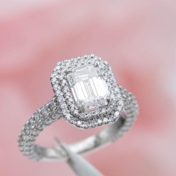 An emerald cut diamond engagement ring with a double halo and pave on every side of the band.