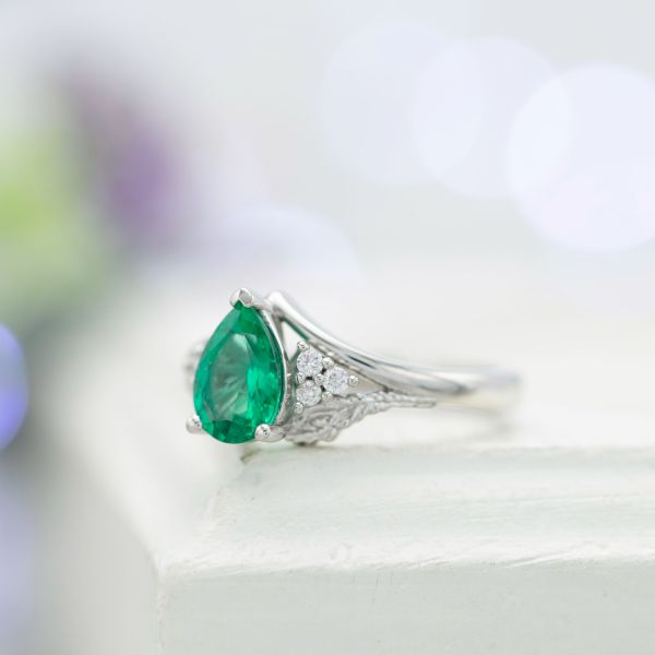 Emerald engagement ring with accent diamonds and peacock feathers.