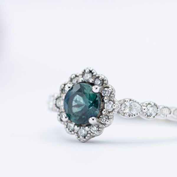 A dusky blue-green sapphire center stone set in a vintage-inspired white gold engagement ring.