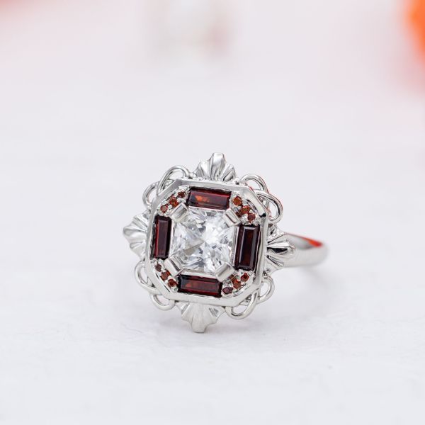 We designed this Art Deco-influenced engagement ring with an asscher cut white sapphire and red garnet accents.