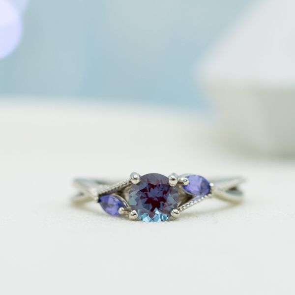 Alexandrite engagement ring with marquise tanzanite side stones in a curving bypass setting.