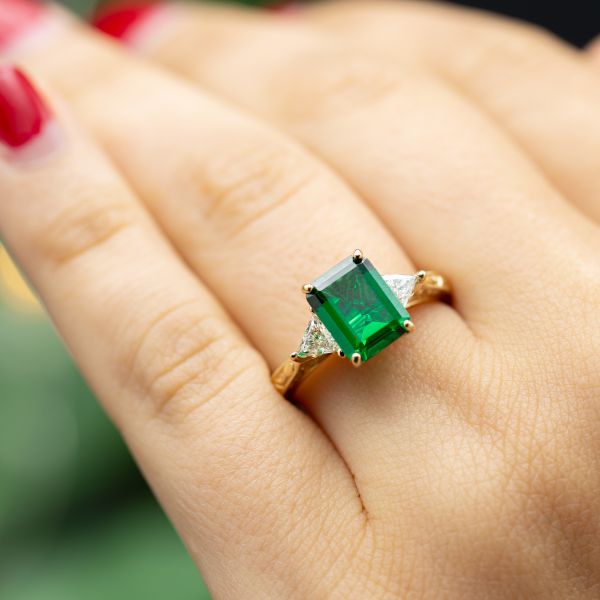 This gorgeous three-stone setting uses trillion cut diamonds to taper from the emerald center stone into the delicate band.