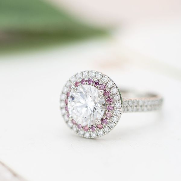 An inner halo of pink diamonds creates subtle contrast between the sparkle of the diamond center stone and the outer diamond halo.