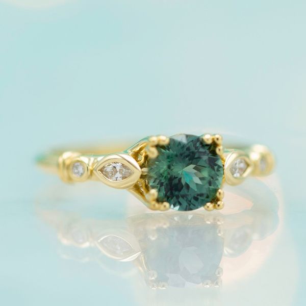 Bluish-green sapphire engagement ring with a gold, triple prong setting.