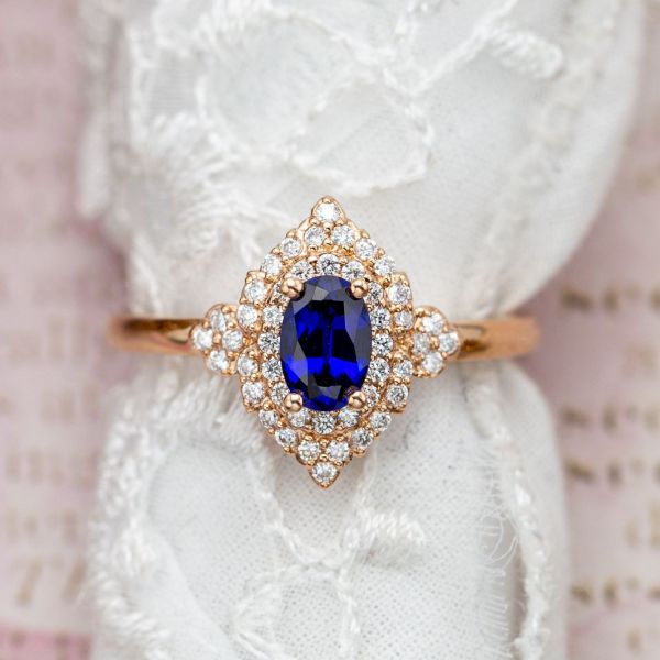 A vintage-inspired blue sapphire engagement ring with a stylized double-halo of diamonds around the lab-created center stone.